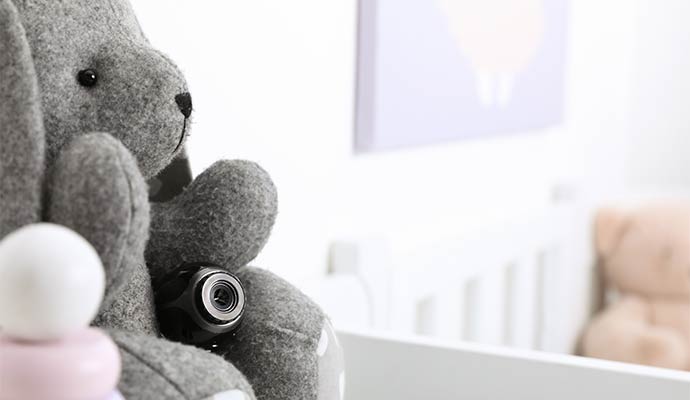A small black hidden camera tucked into a grey stuffed animal in a nursery setting