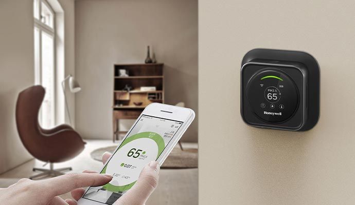 Smart thermostat controlled using mobile app Expert adjusting temperature using a mobile app while the thermostat displays the current temperature