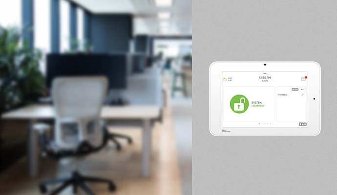 Office setting featuring a wall-mounted interactive panel displaying the security system armed status