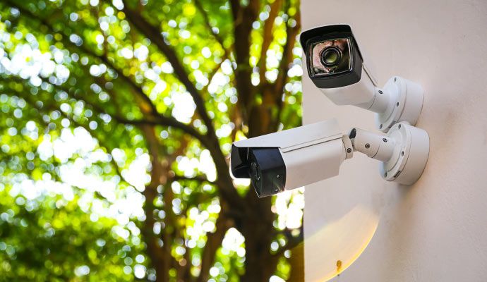 Two outdoor bullet security cameras mounted on a wall with green trees in the background