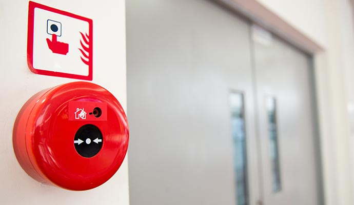 Red fire alarm call point mounted on a wall near double doors for emergency alert