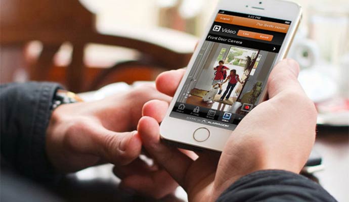 A person holding a smartphone displaying a live front door camera feed through a mobile security app