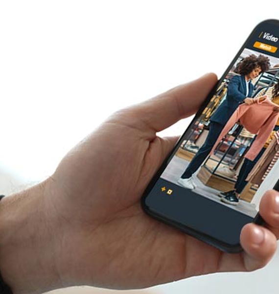 Business owner monitoring clothing store security camera footage on smartphone